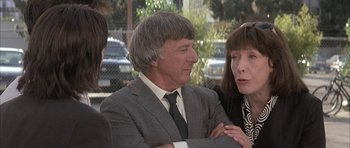 Movie still from “I Heart Huckabees” (2004), directed by David O. Russell – A man in a gray suit is talking to two other people; Close Up shot, Over the shoulder angle