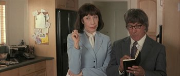 Movie still from “I Heart Huckabees” (2004), directed by David O. Russell – A woman in a blue suit smoking a cigarette in front of a man in a black suit; Close Up shot, High angle
