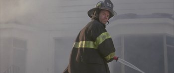 Movie still from “I Heart Huckabees” (2004), directed by David O. Russell – A fireman holding a fire hose while standing in a building; Medium shot, Low angle