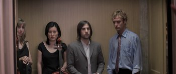 Movie still from “I Heart Huckabees” (2004), directed by David O. Russell – A man and two women standing next to each other; Medium shot, Low angle