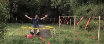 Movie still from “I Heart Huckabees” (2004), directed by David O. Russell – A man sitting on top of a rock in the grass; Wide shot, High angle