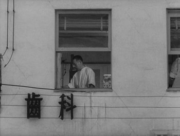 Movie still from “I Live in Fear” (1955), directed by Akira Kurosawa – A man looking out of a window on the side of a building; Wide shot, Low angle