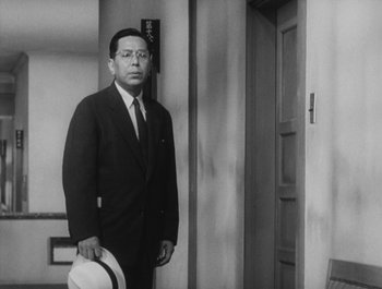 Movie still from “I Live in Fear” (1955), directed by Akira Kurosawa – A man in a suit and tie holding a white hat; Medium shot, Low angle