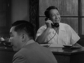 Movie still from “I Live in Fear” (1955), directed by Akira Kurosawa – A man sitting at a table talking on a phone; Medium shot, High angle
