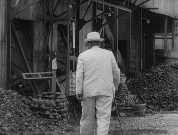 Movie still from “I Live in Fear” (1955), directed by Akira Kurosawa – An older man in a hat and a suit walking in front of a building; Medium shot, Over the shoulder angle