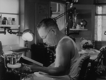 Movie still from “I Live in Fear” (1955), directed by Akira Kurosawa – A man sitting in a chair reading a book; Medium shot, Low angle
