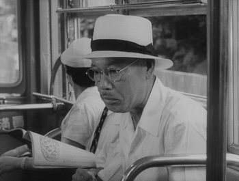 Movie still from “I Live in Fear” (1955), directed by Akira Kurosawa – An older man sitting on a bus reading a newspaper; Close Up shot, Low angle