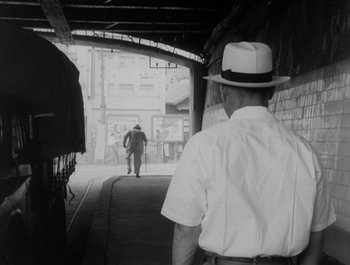 Movie still from “I Live in Fear” (1955), directed by Akira Kurosawa – A black and white photo of a man walking down a street; Wide shot, Over the shoulder angle