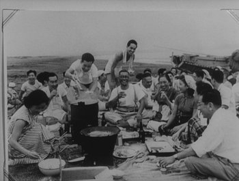 Movie still from “I Live in Fear” (1955), directed by Akira Kurosawa – A group of people sitting around a table with food on top of it; Wide shot, High angle