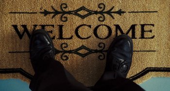 Movie still from “I Love You Phillip Morris” (2009), directed by John Requa – A man standing on a welcome mat with his feet on the floor; Wide shot, Low angle