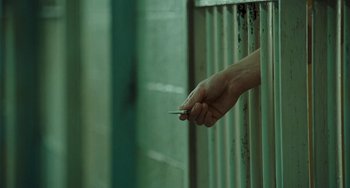 Movie still from “I Love You Phillip Morris” (2009), directed by John Requa – A hand is holding a cigarette sticking out of a jail cell; Extreme Close Up shot, High angle
