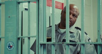 Movie still from “I Love You Phillip Morris” (2009), directed by John Requa – A police officer standing behind bars in a jail cell; Medium shot, Over the shoulder angle