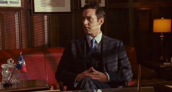 Movie still from “I Love You Phillip Morris” (2009), directed by John Requa – A man in a suit sitting in front of a table; Medium shot, Over the shoulder angle