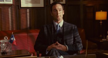 Movie still from “I Love You Phillip Morris” (2009), directed by John Requa – A man sitting at a table in a suit and tie; Medium shot, Low angle