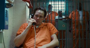 Movie still from “I Love You Phillip Morris” (2009), directed by John Requa – A man sitting in front of a jail cell on the phone; Medium shot, Low angle