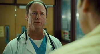 Movie still from “I Love You Phillip Morris” (2009), directed by John Requa – A man wearing a white lab coat with a stethoscope around his neck; Close Up shot, Over the shoulder angle