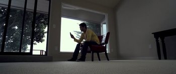 Movie still from “I Melt with You” (2011), directed by Mark Pellington – A man sitting on a chair in a room; Wide shot, Low angle