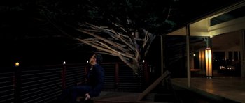 Movie still from “I Melt with You” (2011), directed by Mark Pellington – A man sitting on a bench in front of a large tree; Wide shot, Low angle
