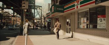Movie still from “I Origins” (2014), directed by Mike Cahill – A man walking down the sidewalk in front of a 7 - eleven store; Wide shot, Over the shoulder angle