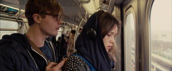 A man and a woman on a train with ear phones on