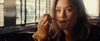 A woman holding a spoon in her mouth while sitting at a table in a restaurant