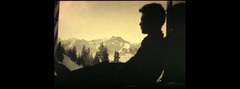 Movie still from “I Stand Alone” (1998), directed by Gaspar Noé – A man sitting in front of a window with a view of a mountain; Medium shot, High angle