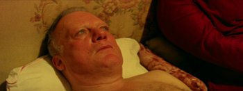 Movie still from “I Stand Alone” (1998), directed by Gaspar Noé – An older man laying on a bed with a hand on his chest; Close Up shot, High angle