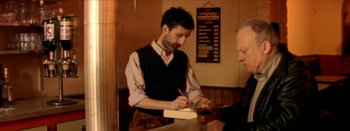Movie still from “I Stand Alone” (1998), directed by Gaspar Noé – A man is writing something on a piece of paper; Medium shot, Over the shoulder angle