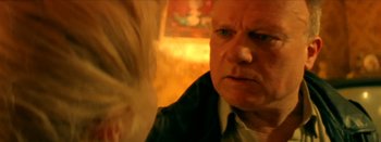 Movie still from “I Stand Alone” (1998), directed by Gaspar Noé – An older man looking at the camera in a dimly - lit room; Close Up shot, Over the shoulder angle