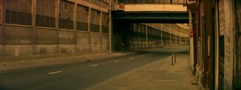 Movie still from “I Stand Alone” (1998), directed by Gaspar Noé – A person walking down a street under an overpass; Extreme Wide shot, High angle