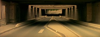 Movie still from “I Stand Alone” (1998), directed by Gaspar Noé – A person standing on the side of a road near a tunnel; Extreme Wide shot, High angle