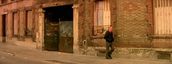 Movie still from “I Stand Alone” (1998), directed by Gaspar Noé – A man walking down the sidewalk in front of a building; Wide shot, Low angle