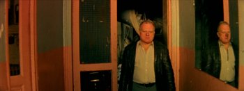 Movie still from “I Stand Alone” (1998), directed by Gaspar Noé – An older man standing in front of an open door; Medium shot, Low angle