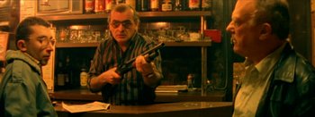 Movie still from “I Stand Alone” (1998), directed by Gaspar Noé – A man sitting at a counter holding a gun; Medium shot, Low angle