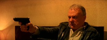 Movie still from “I Stand Alone” (1998), directed by Gaspar Noé – An older man wearing a leather jacket holding a gun; Close Up shot, Low angle