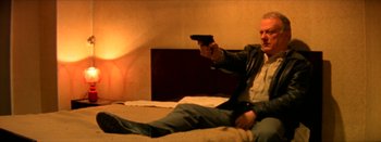 Movie still from “I Stand Alone” (1998), directed by Gaspar Noé – A man sitting on a bed holding a gun in his hand; Medium shot, Low angle