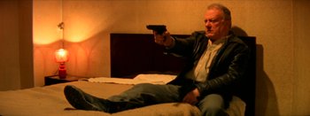 Movie still from “I Stand Alone” (1998), directed by Gaspar Noé – A man sitting on a bed holding a gun; Medium shot, High angle