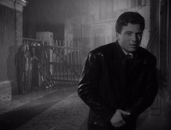 Movie still from “I Vitelloni” (1953), directed by Federico Fellini – A black and white photo of a man in a raincoat; Medium shot, Low angle
