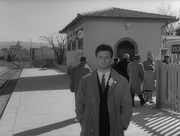 Movie still from “I Vitelloni” (1953), directed by Federico Fellini – A black and white photo of a man standing in front of a building; Medium shot, Low angle