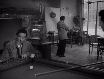 Movie still from “I Vitelloni” (1953), directed by Federico Fellini – A man sitting at a pool table in front of a woman; Wide shot, High angle