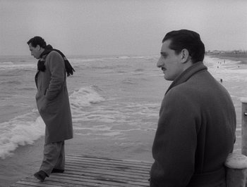 Movie still from “I Vitelloni” (1953), directed by Federico Fellini – Two men are standing on a pier near the ocean; Wide shot, Low angle