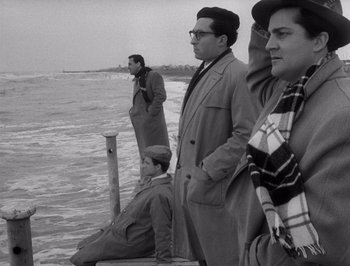 Movie still from “I Vitelloni” (1953), directed by Federico Fellini – A group of men standing on a pier next to the ocean; Medium shot, Low angle