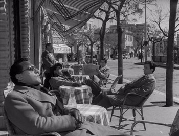 Movie still from “I Vitelloni” (1953), directed by Federico Fellini – A black and white photo of people sitting at tables outside; Wide shot, High angle