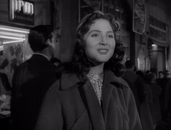 Movie still from “I Vitelloni” (1953), directed by Federico Fellini – A woman in a coat standing in a crowd of people; Medium shot, Low angle