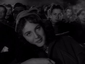 Movie still from “I Vitelloni” (1953), directed by Federico Fellini – A black - and - white photo of a woman in a crowd of people; Close Up shot, Low angle