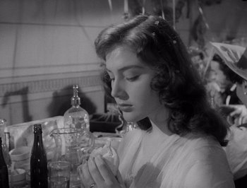 Movie still from “I Vitelloni” (1953), directed by Federico Fellini – A young woman sitting in front of a wine bottle; Close Up shot, Low angle