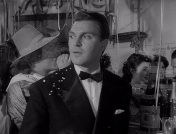Movie still from “I Vitelloni” (1953), directed by Federico Fellini – A man in a suit and a bow tie standing in front of other people; Close Up shot, Low angle