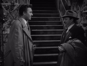 Movie still from “I Vitelloni” (1953), directed by Federico Fellini – Two men in trench coats and hats talking on the stairs; Medium shot, High angle
