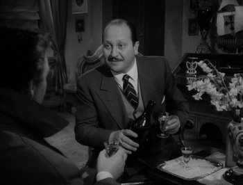 Movie still from “I Vitelloni” (1953), directed by Federico Fellini – A man sitting at a table with a bottle of wine; Medium shot, Over the shoulder angle