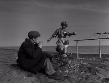 Movie still from “I Vitelloni” (1953), directed by Federico Fellini – A man sitting on the ground next to a statue of a woman; Wide shot, Low angle